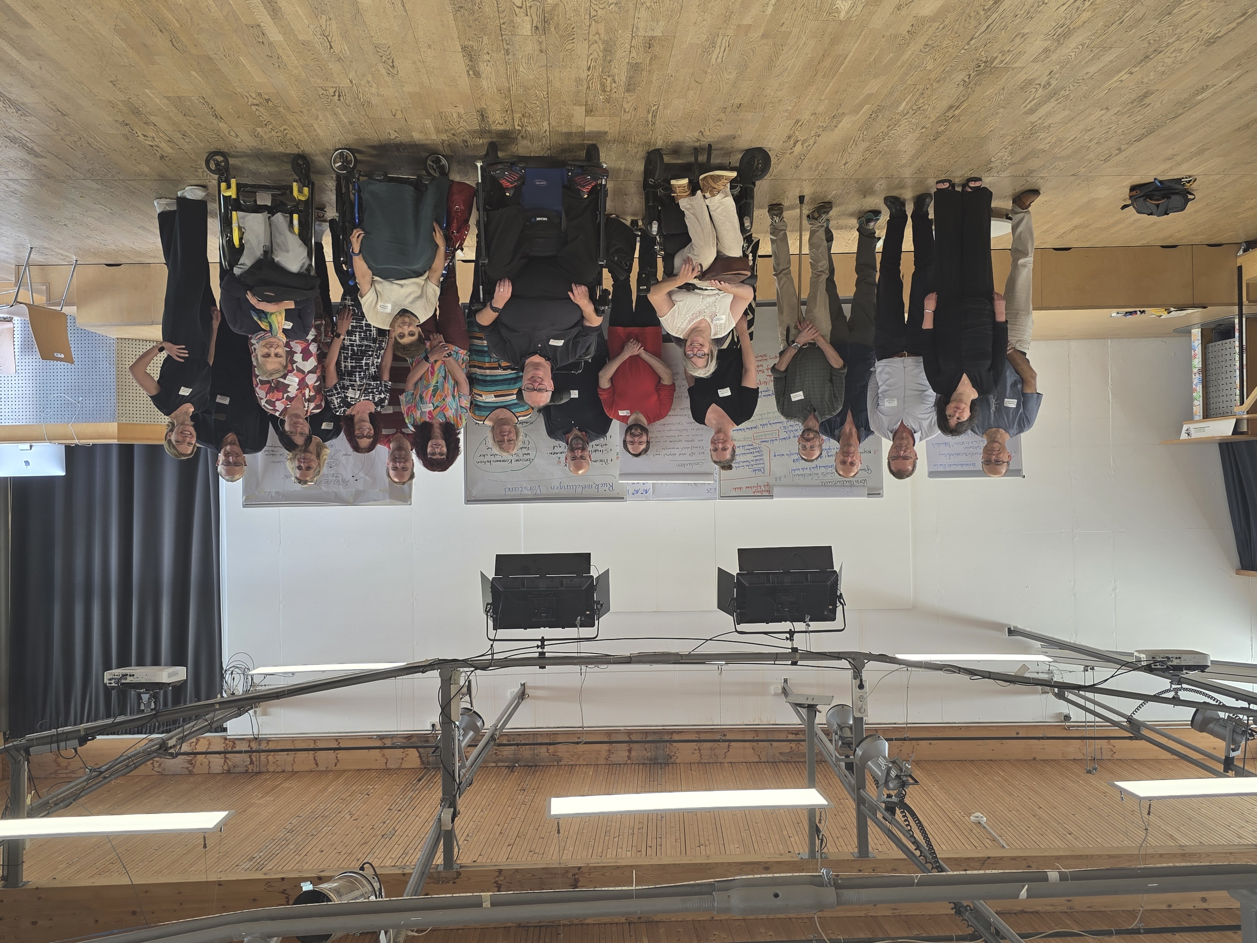 Gruppenfoto von Teilnehmenden einer Sitzung, einige im Rollstuhl, vor Pinnwänden in einem hellen Raum.