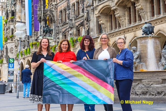 Hintergrund Rathaus, 5 Personen halten die Disability Pride Fahne. Von links nach rechts: Daniela Maier, 3. Bürgermeisterin Verena Dietl, Nadja Rackwitz, Cornelia von Pappenheim und Sofie Langmeier