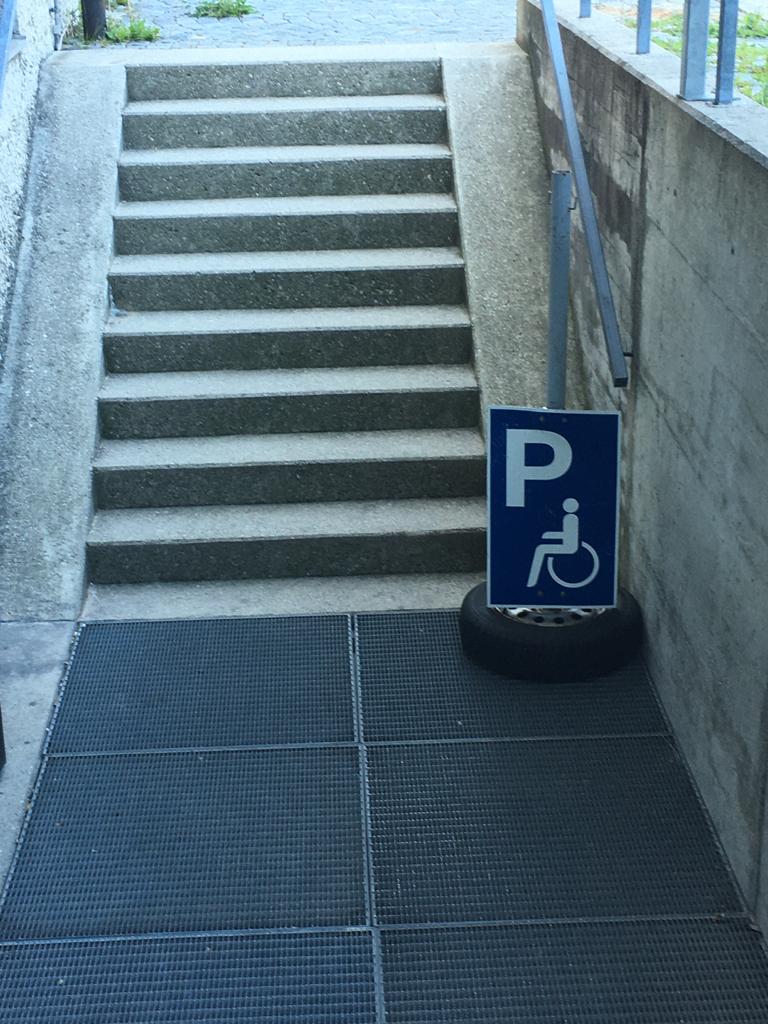 Treppe vor der ein Schild Behindertenparkplatz steht